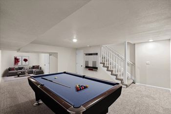 A pool table is in the middle of a room with a staircase on the right.